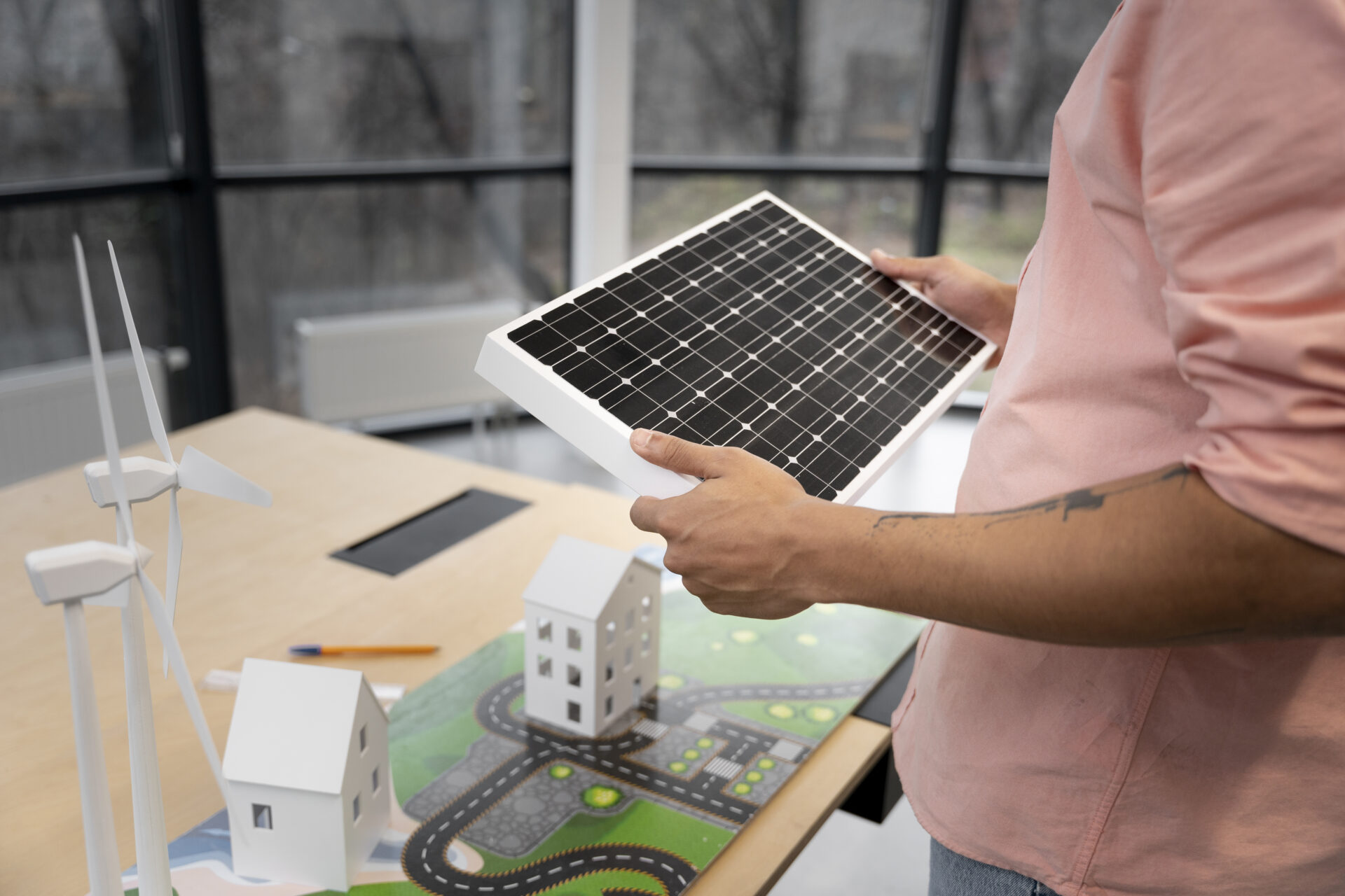 makety obnoviteľných zdrojov energie na drevenom stole, muž drží v ruke fotovoltické panely, na stole sú aj veterné turbíny, žiadosť o dotácie na fotovoltiku